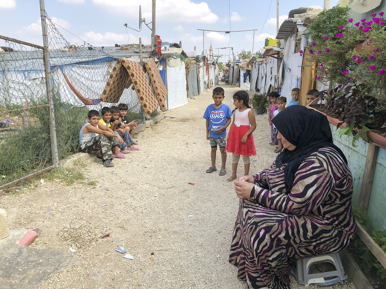 Eine Frau und mehrere Kinder sitzen und stehen auf einem Weg durch ein Camp für syrische Flüchtlinge im Libanon.