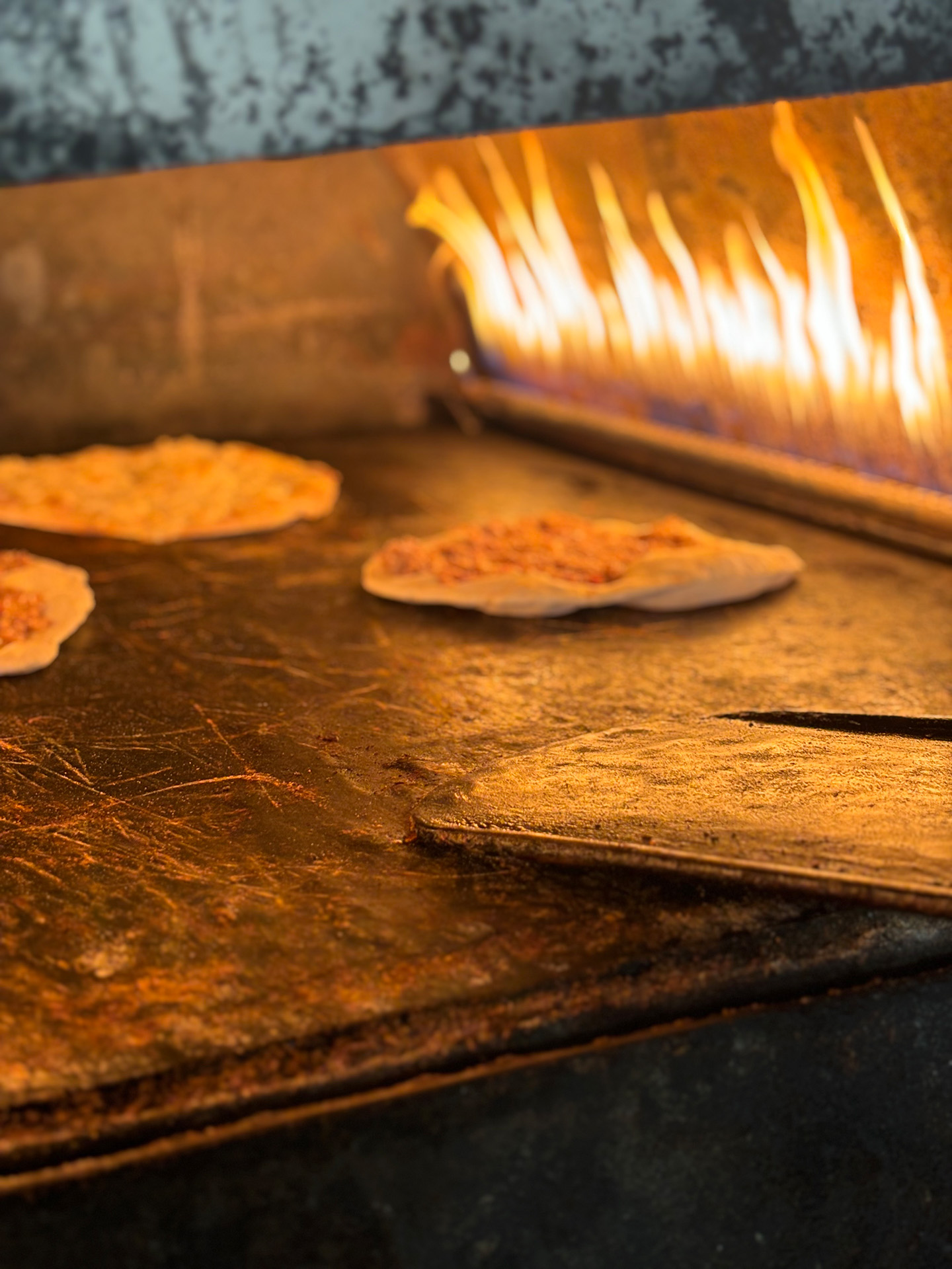 Ein befeuerter Backofen mit mehreren flach ausgerollten Laiben Brot.