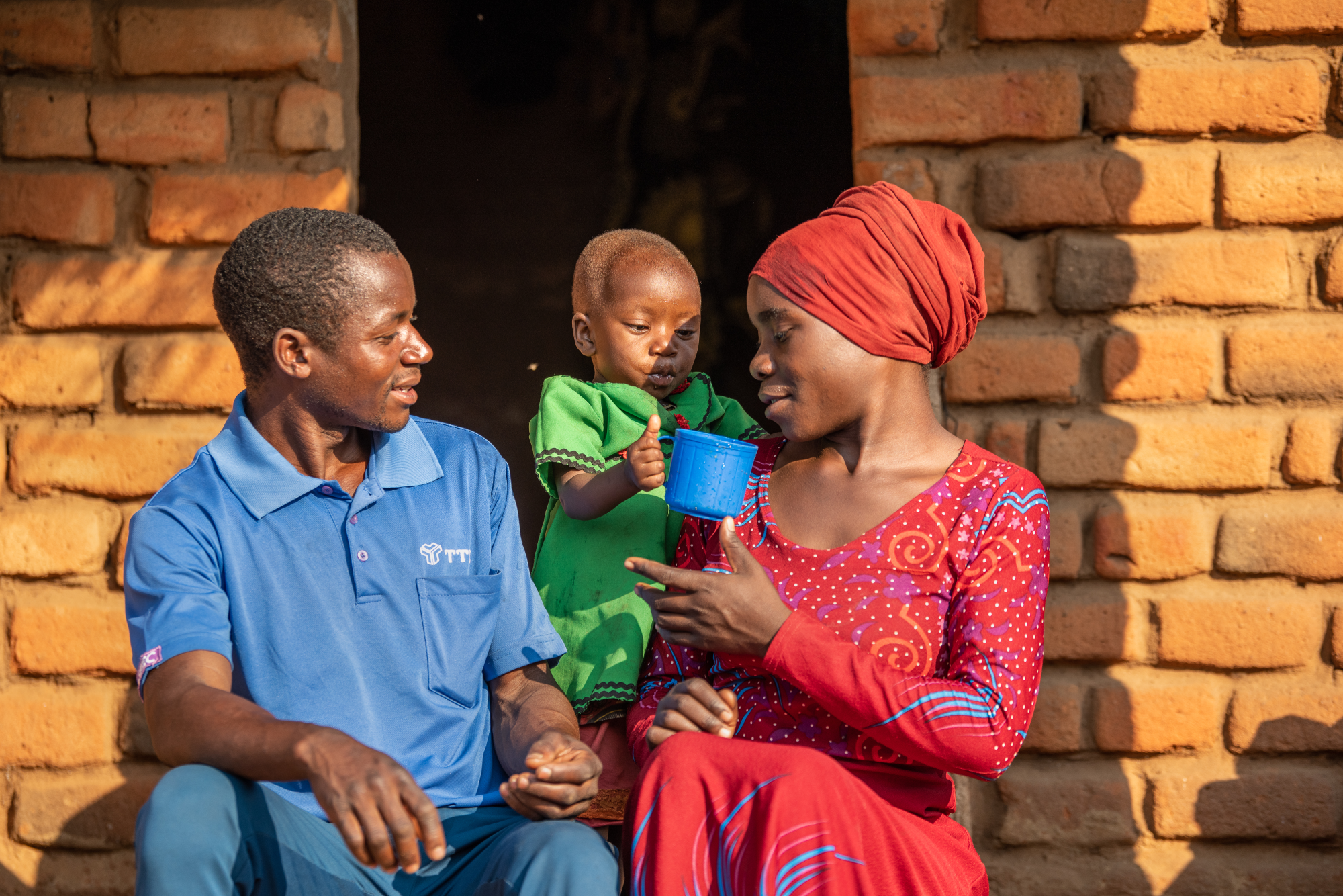 Jamila Liwanda und ihr Mann Sharif sitzen mit ihrer Tochter Sumini vor ihrem Haus in Malawi