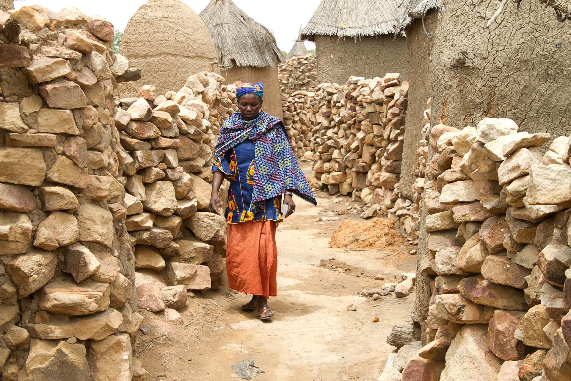 Eine Frau in Mali läuft zwischen Lehmhütten entlang.