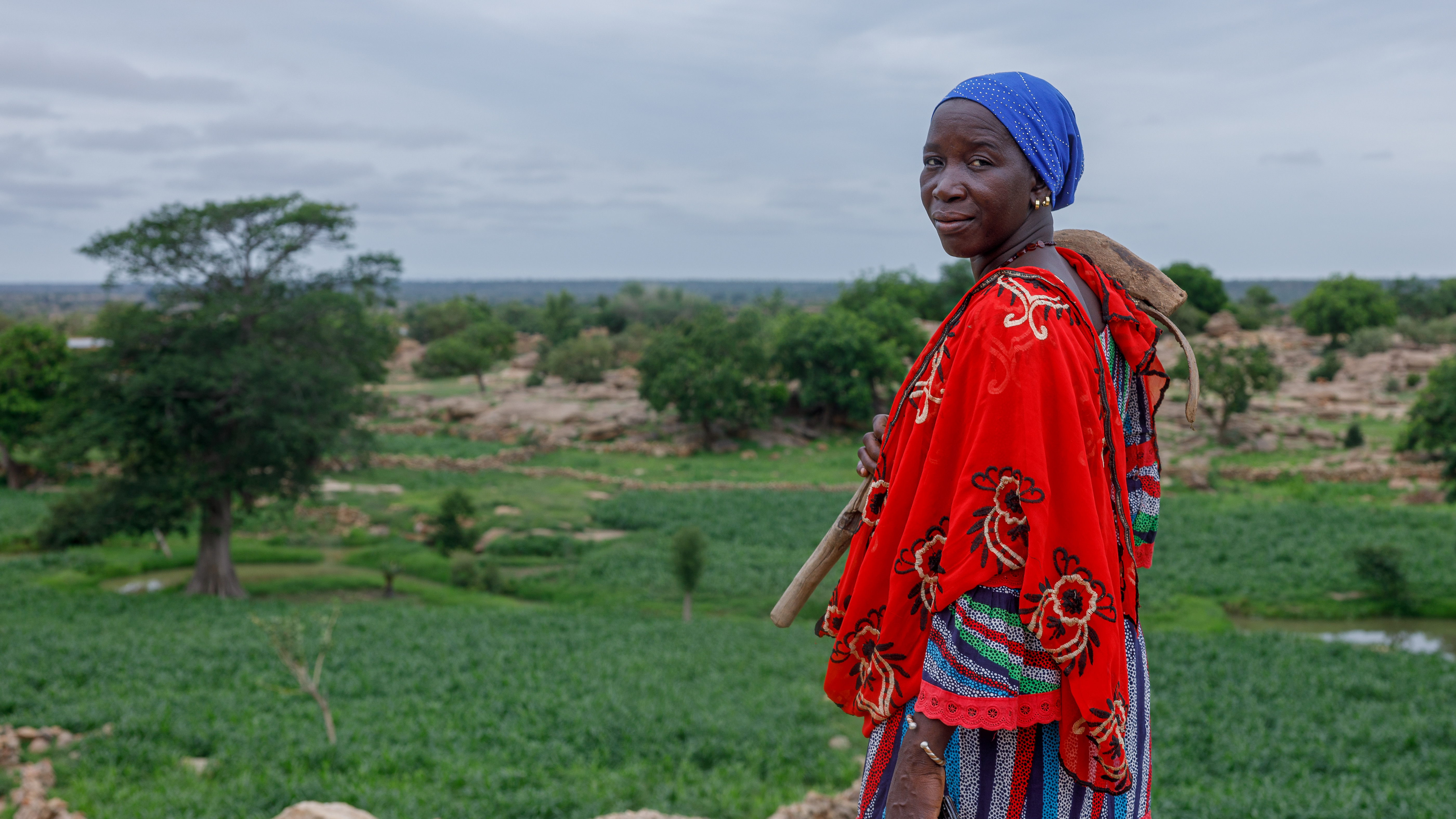 Eine Frau in farbenfroher Kleidung steht mit einem landwirtschaftlichen Werkzeug auf einem Feld in Mali.