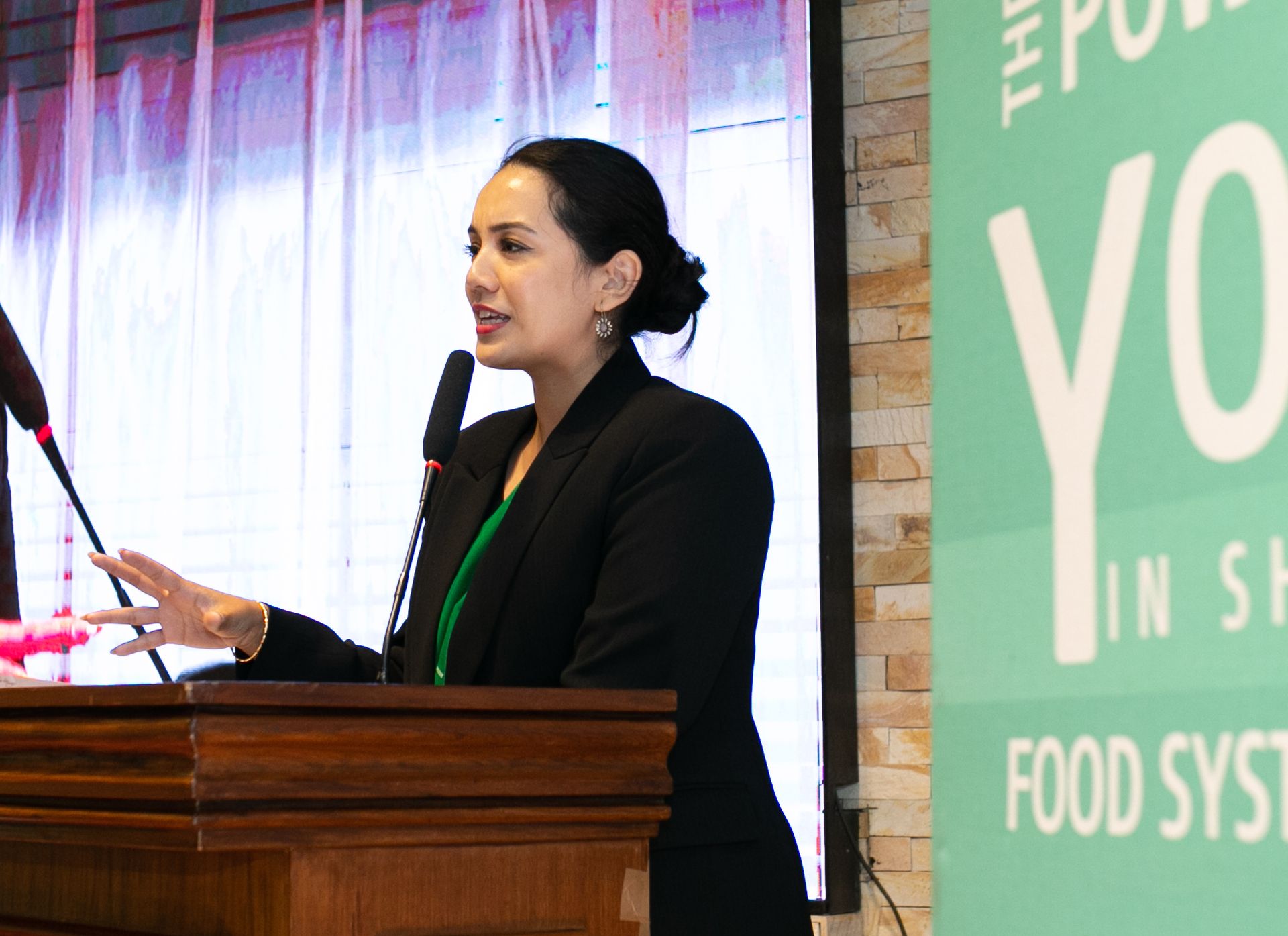 Eine Frau hinter einem Rednerpult spricht in ein Mikrophon.