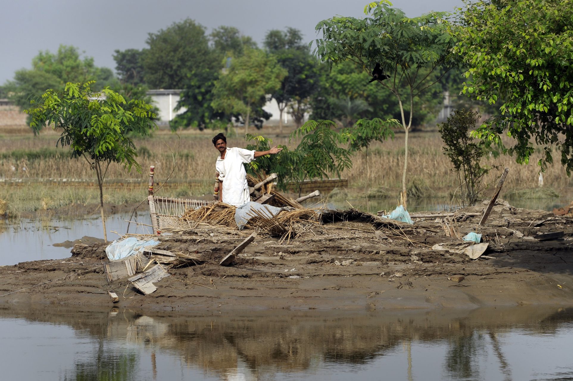 Ein Mann steht auf einem von Wasser umgebenen Stück Land und zeigt auf zerstörte Haushaltsgegenstände.