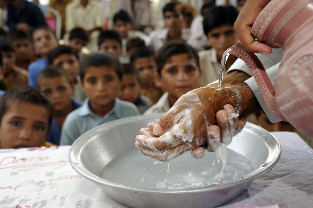 Hände voller Schaum über einer Schüssel. Im Hintergrund sieht man Kinder, die zuschauen.