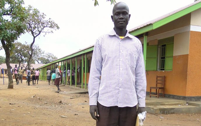 Akoy steht auf dem Schulhof, hinter ihm befindet sich das Schulgebäude.
