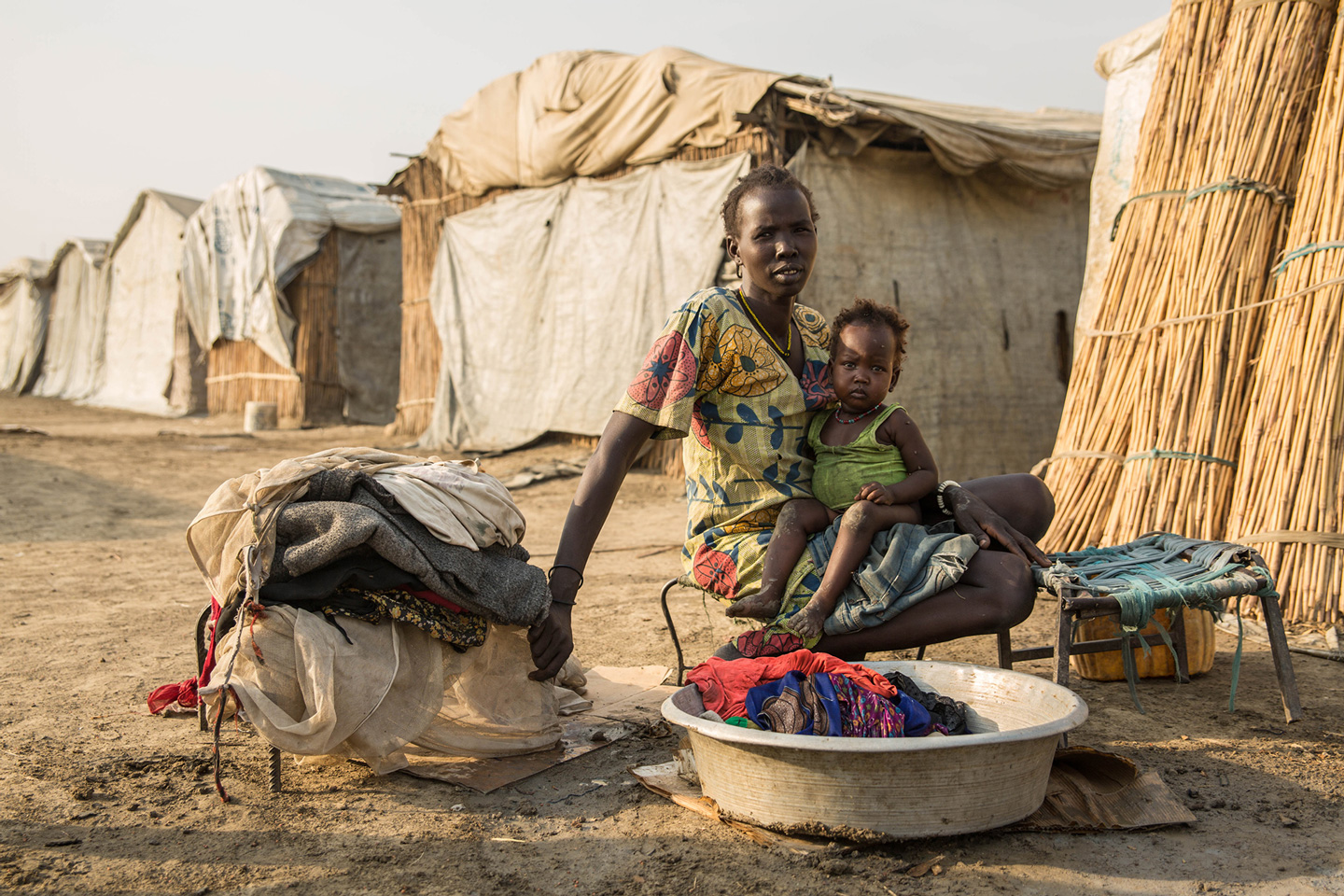 Eine Frau sitzt mit ihrem Baby auf dem Schoß vor einem Waschzuber voller Wäsche.
