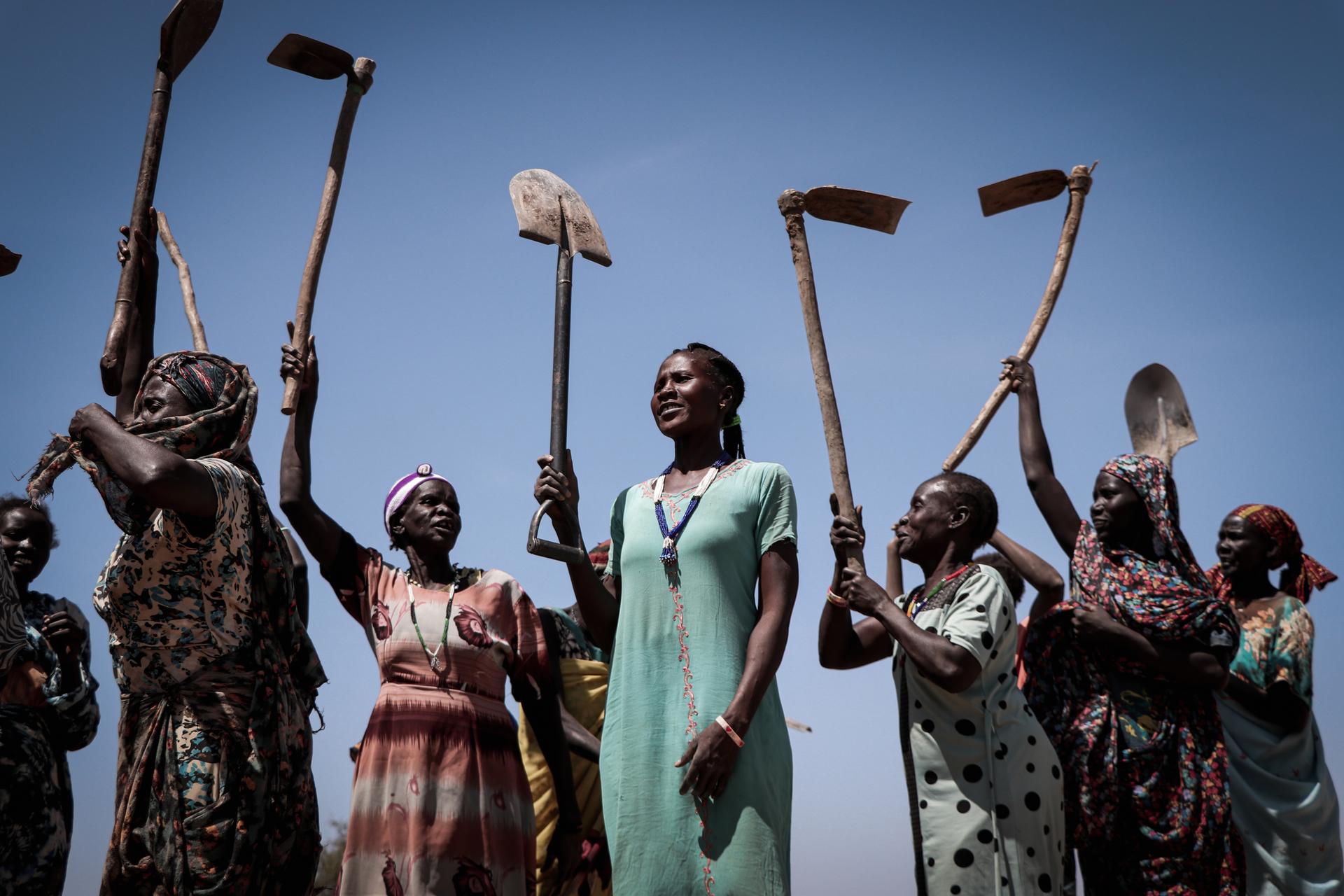 Eine Gruppe Frauen halten Hacken und Schaufeln in die Luft