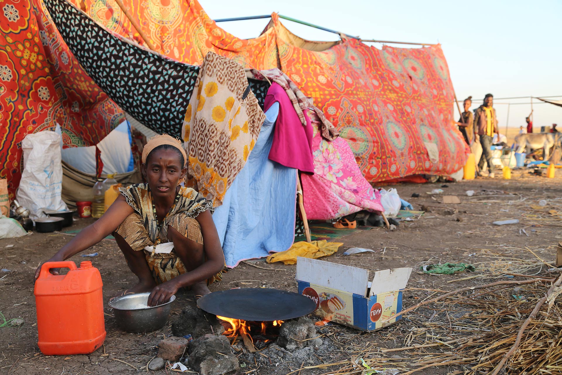 Eine Frau bereitet eine Mahlzeit zu, im Hintergrund sieht man eine provisorische Unterkunft. Foto: WFP
