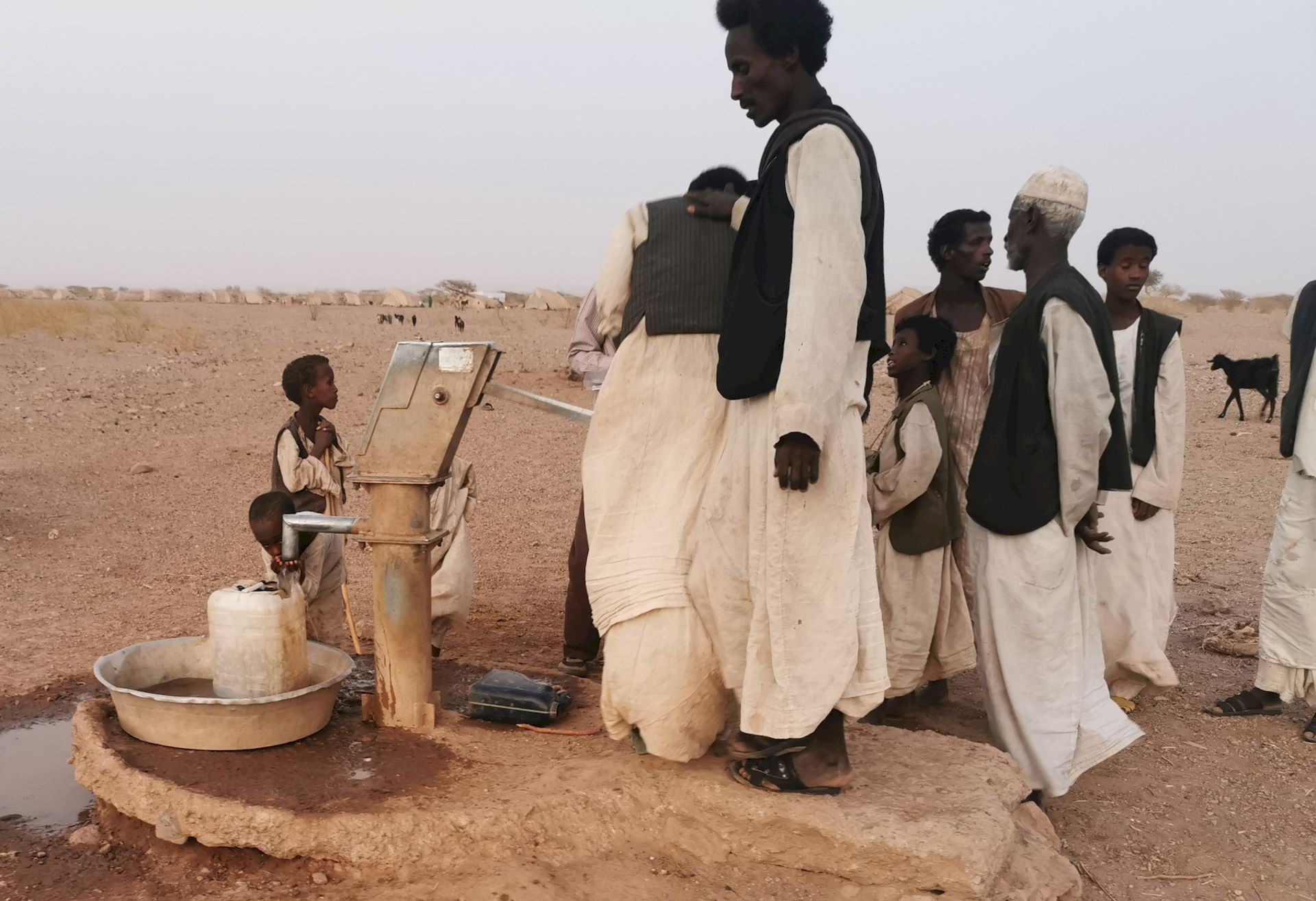 In einer wüstenartigen Landschaft umstehen Männer einen Zapfhahn für Wasser.