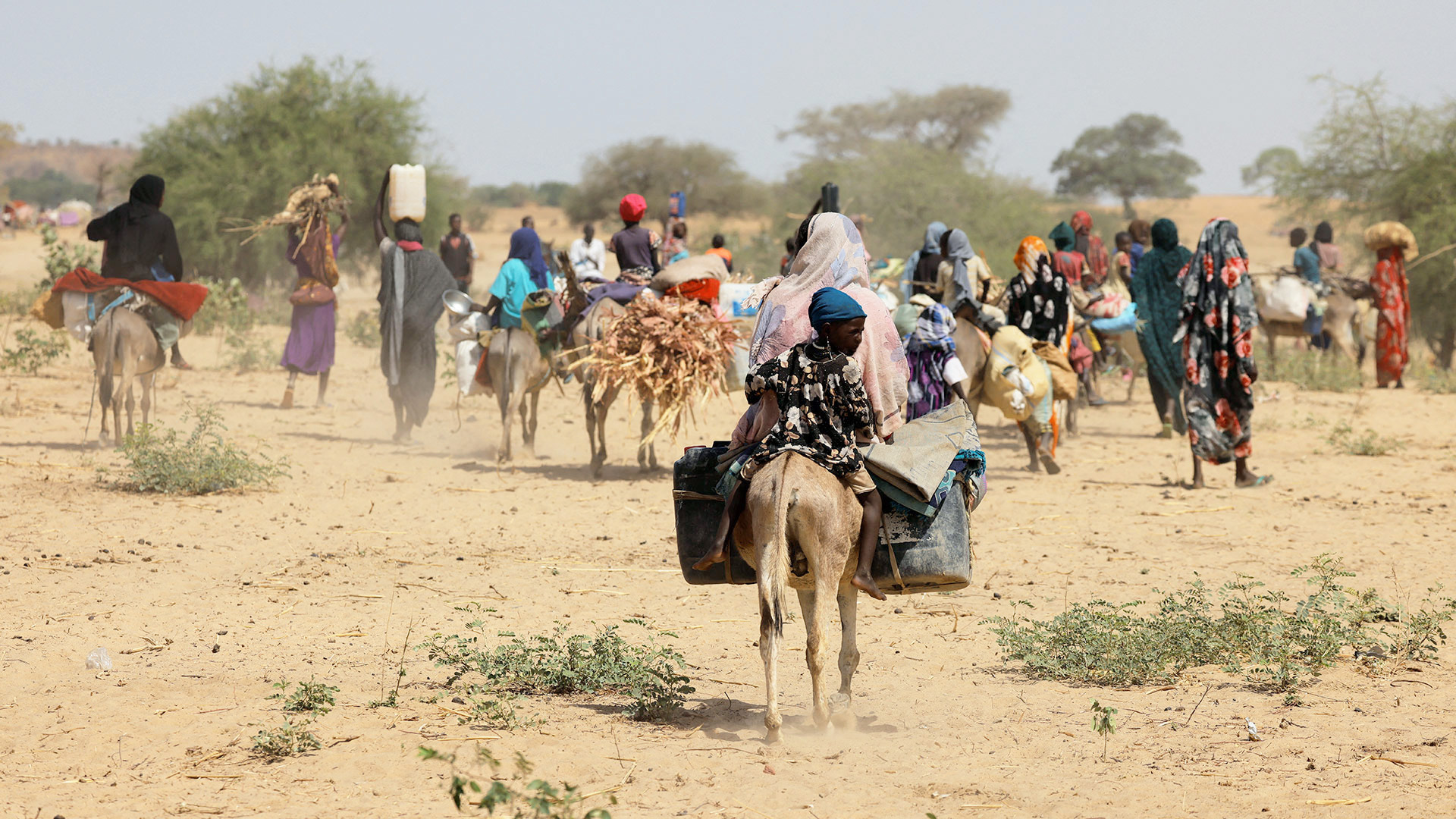 Sudanesische Flüchtlinge, die vor der Gewalt in der Region Darfur geflohen sind, suchen in Goungour, Tschad, vorübergehende Zuflucht. Das Bild zeigt Menschen, die zu Fuß und mit Eseln unterwegs sind und Gepäck tragen.