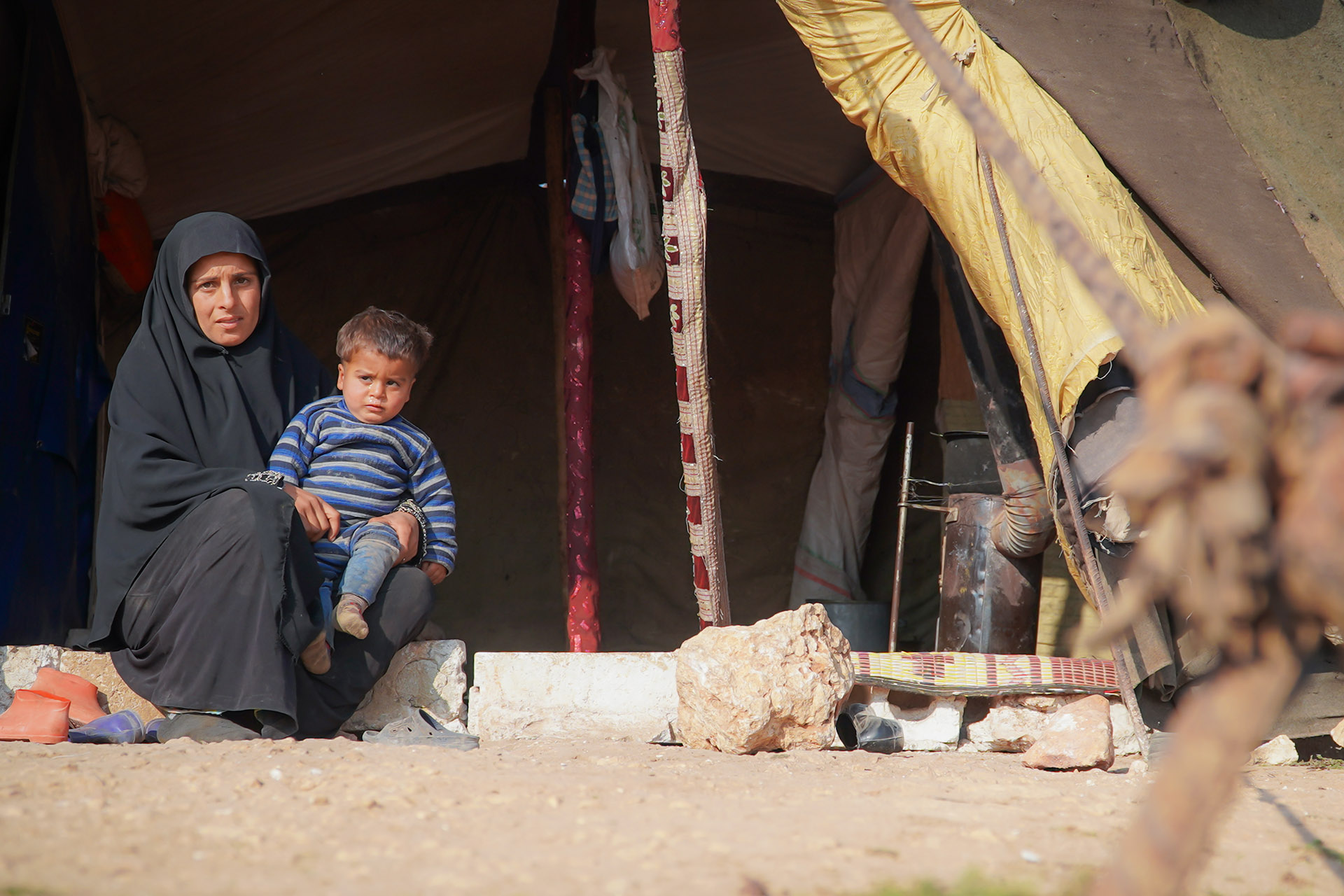 Eine Frau sitzt auf einer Stufe vor einem Zelt. Auf ihrem Schoß sitzt ein Kind.