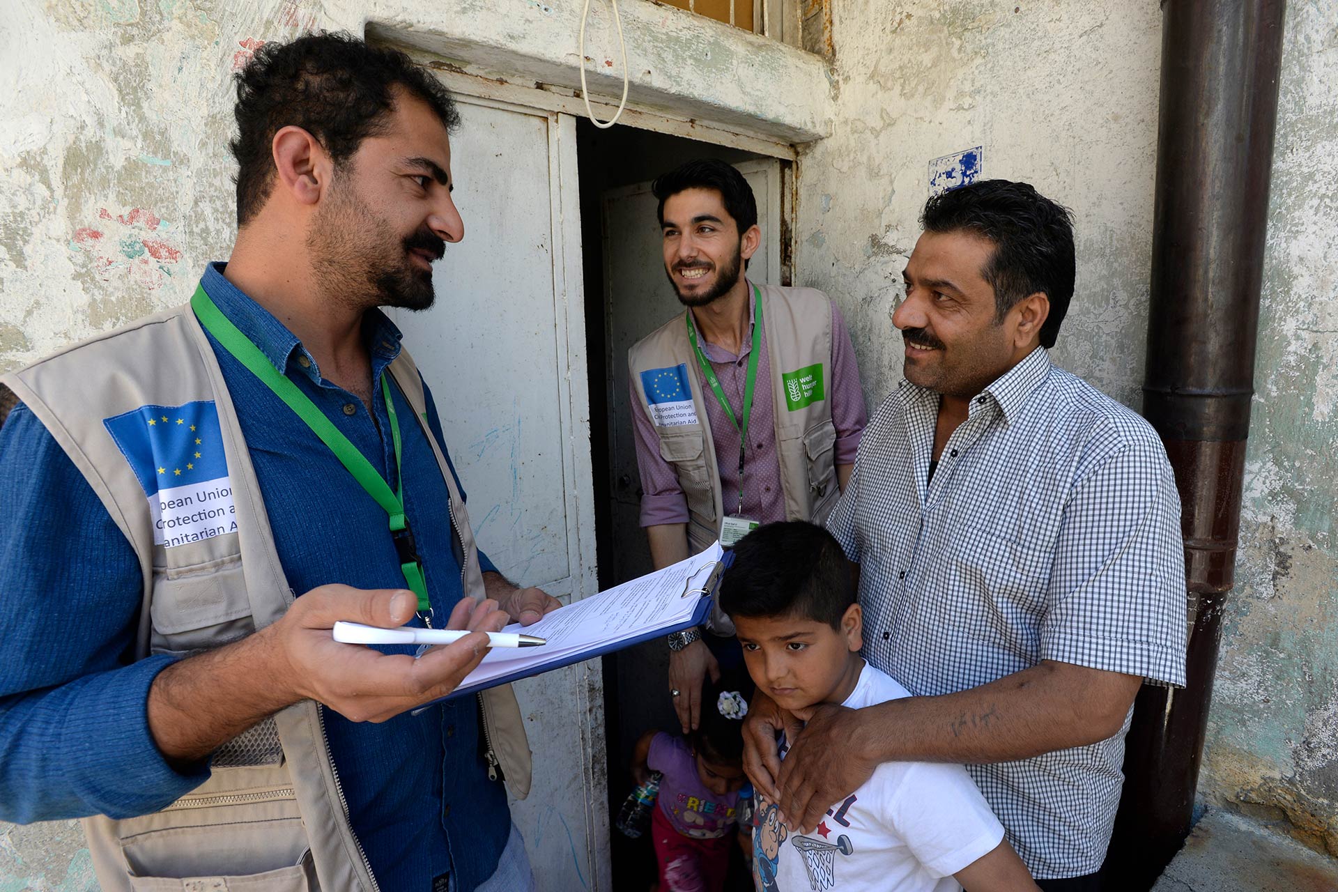 Zwei Welthungerhilfe-Männer reden mit einem Mann und einem kleinen Kind.