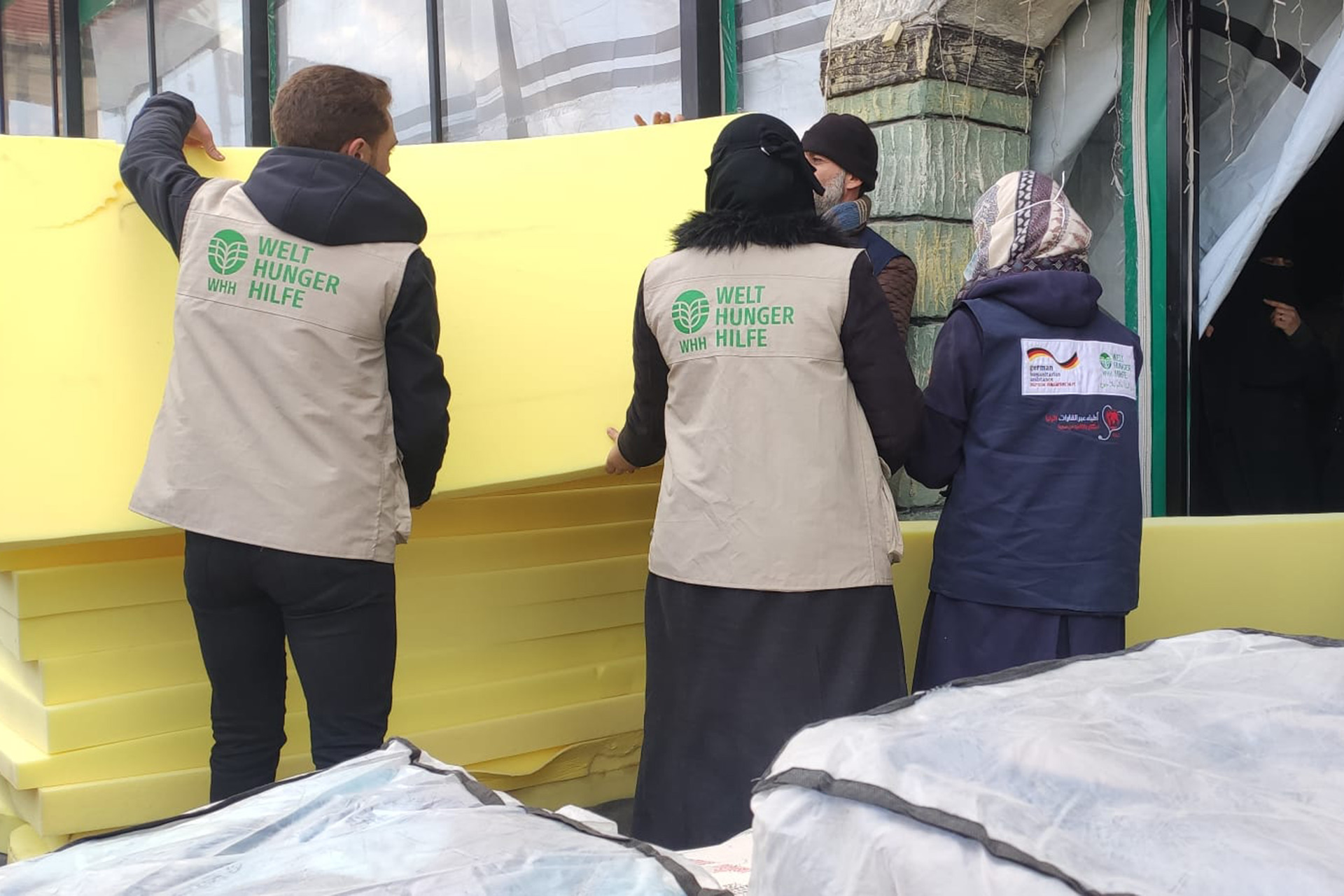 Nothilfe für Menschen in Syrien: Personen in Welthungerhilfe-Weste verteilen Matratzen.