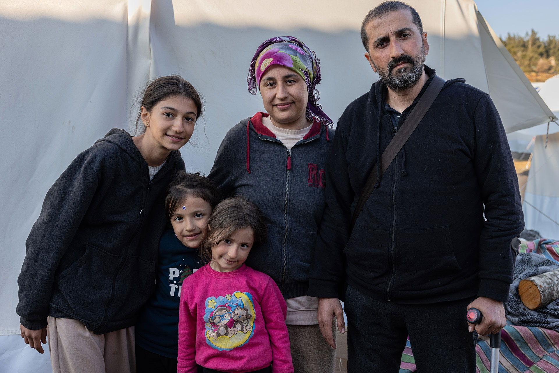 Erdbeben in der Türkei: Eine Familie steht vor einem Zelt, sie alle schauen in die Kamera.
