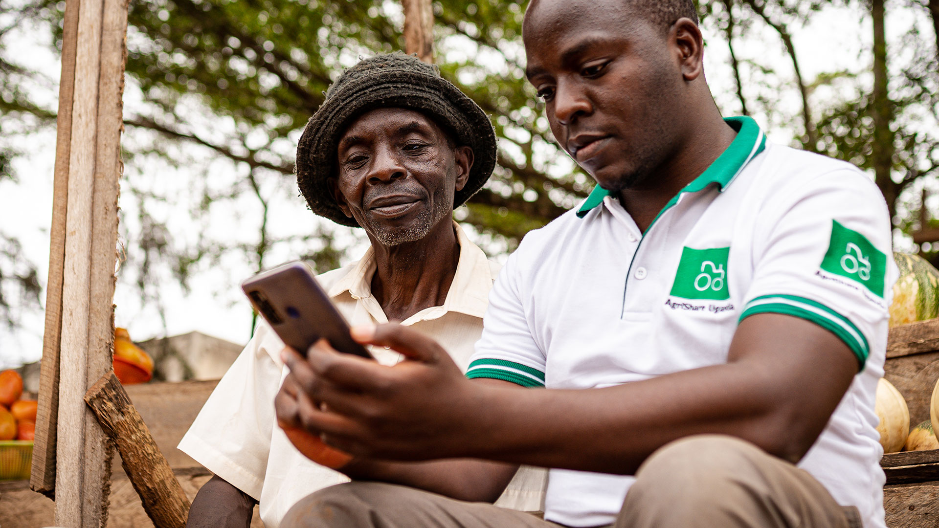 Zwei Kleinbauern schauen in ihr Smartphone und beschäftigen sich mit der Landwirtschafts-App AgriShare, Uganda 2021.