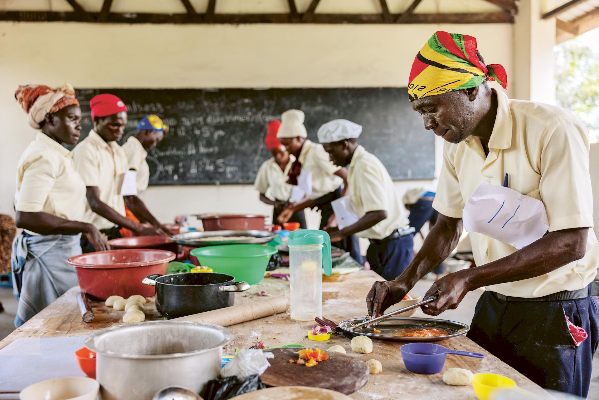 Ein Mann bereitet an einem langen Küchentisch ein Gericht vor.