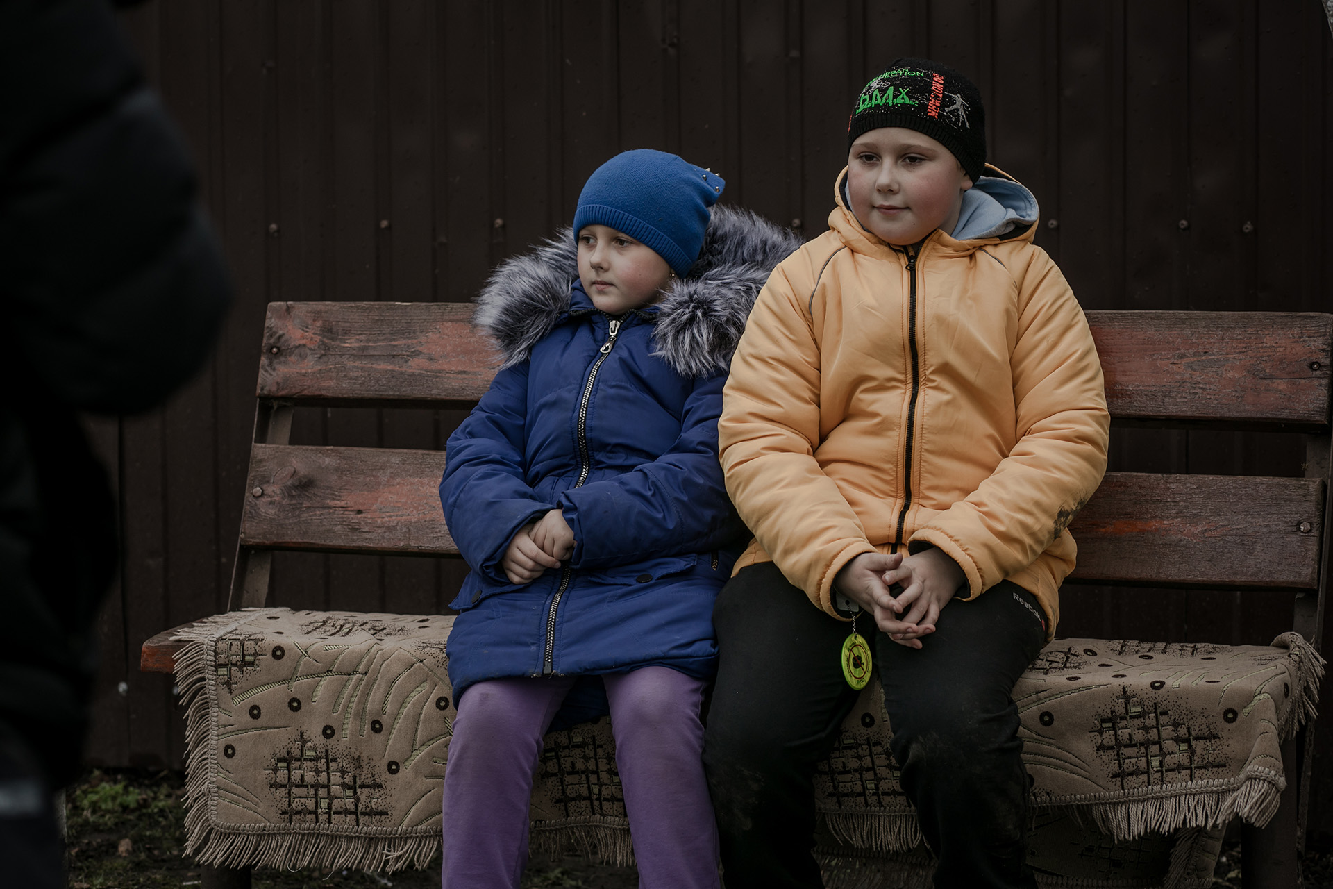 Zwei ukrainische Kinder aus einem Dorf in der Region Charkiw sitzen auf einer Bank