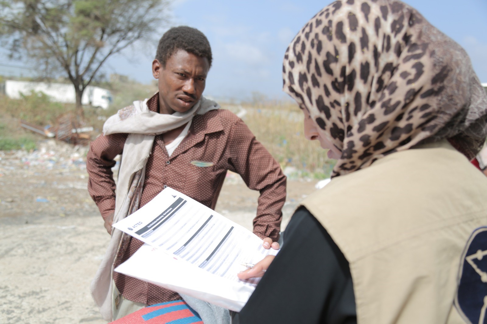 Eine Frau und ein Mann sprechen miteinander. Die Frau hat Papiere in der Hand.