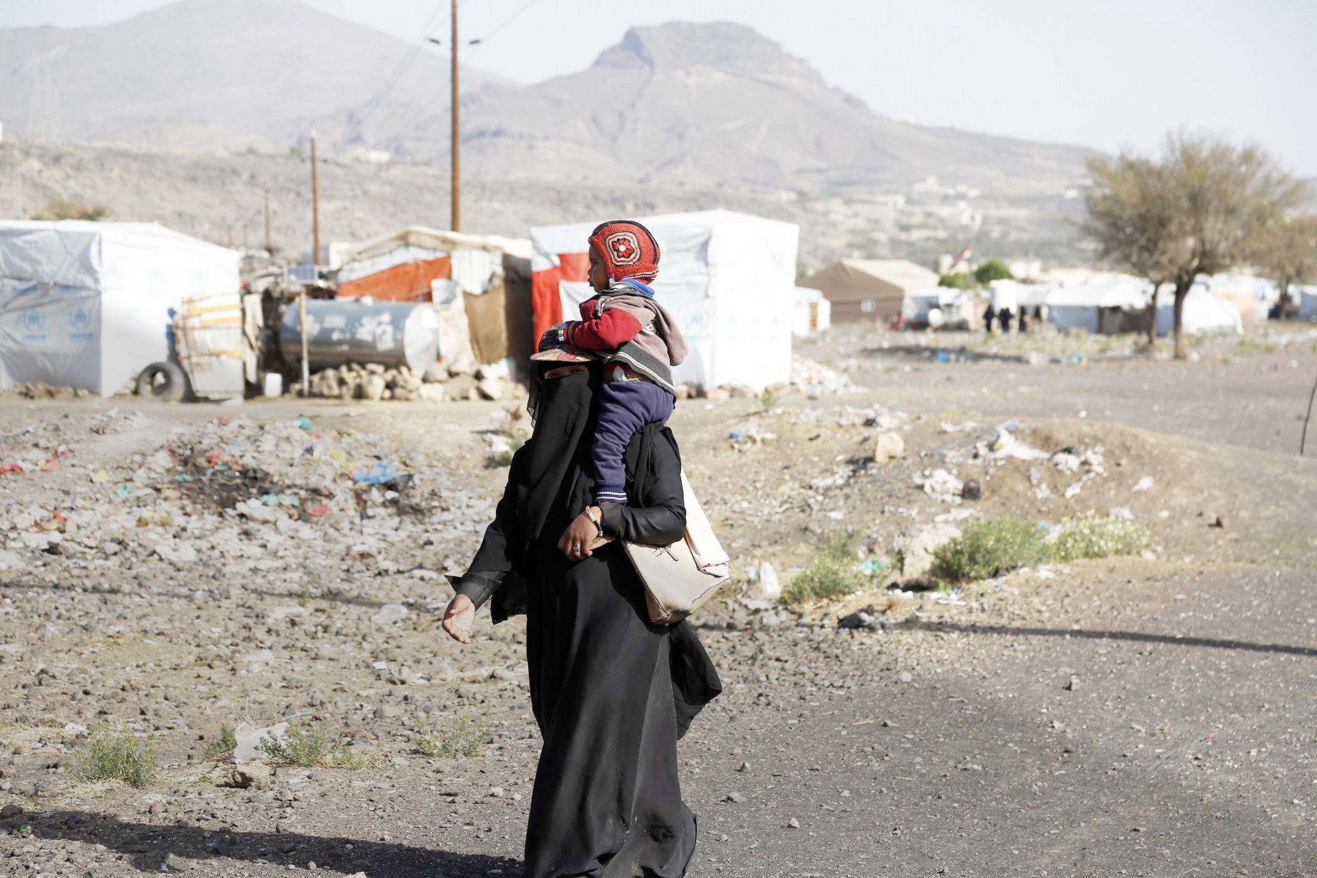Eine Mutter trägt ihr Kind durch das Dharawan Flüchtlingscamp in Sanaa, Jemen. Die Menschen im Camp kämpfen unter schwierigen Bedingungen ums Überleben. 