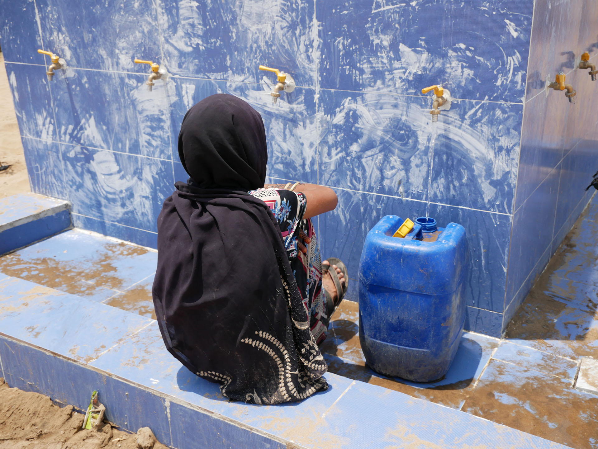 Eine Frau wartet an einer Wasserstelle darauf, dass ihr Kanister mit Trinkwasser voll wird.