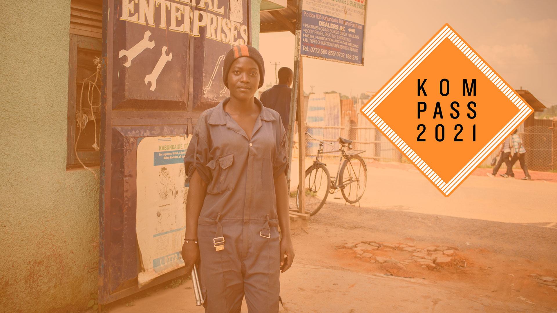 2017-kompass-ausbildung-skill-up-auszubildende-werkstatt-logo_C_lass.jpg Ausbildungsprogramm "Skill up!" in Uganda. Eine Frau Sie trägt einen blauen Overall und hält Werkzeuge in der Hand. Rechts ist das "Kompass 2021" Logo.