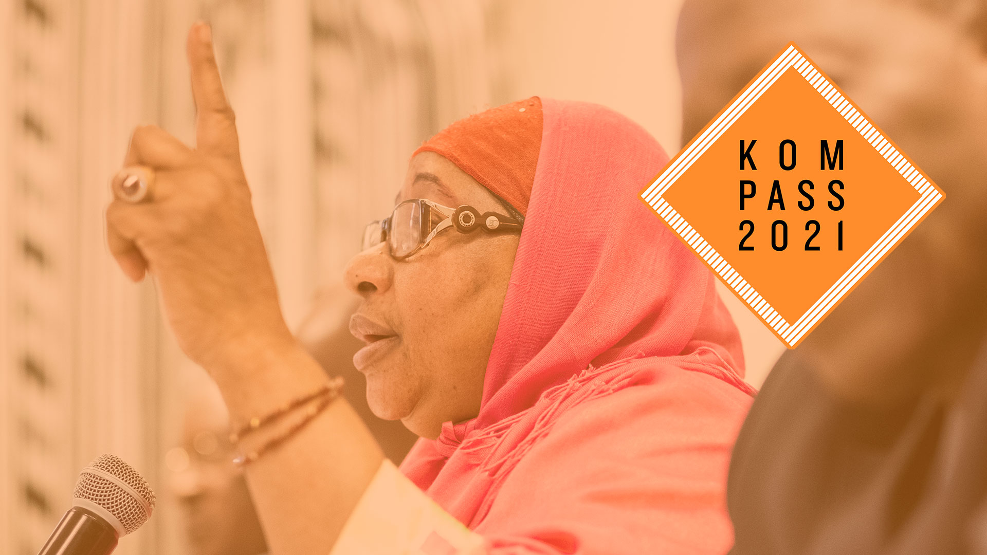 2018-kompass-frau-diskussion-whi-mali-logo_C_pilar.jpg Präsentation des Welthunger-Index. Eine Frau hebt ihre Hand, vor ihr steht ein Mikrofon. Oben rechts ist das Kompass 2021 Logo.