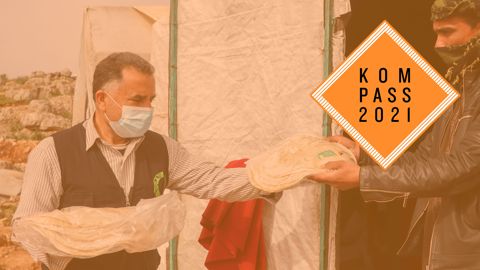 2020-kompass-brot-verteilung-syrien-logo_C_ihsan.jpg Ein Mann händigt einem anderen Mann eine Tüte mit Fladenbrot. Oben rechts ist das Kompass 2021 Logo.