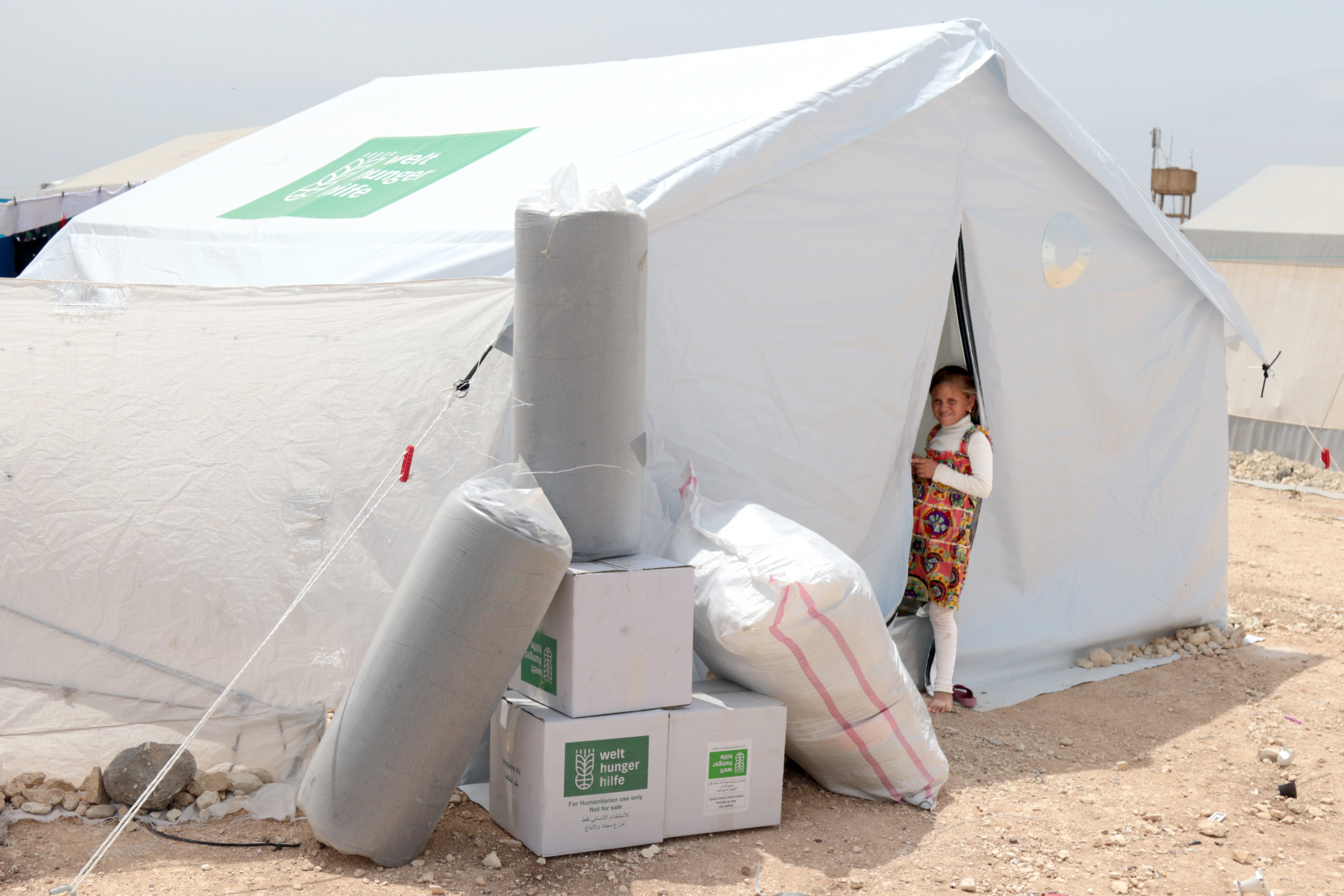 Ein weißes Zelt mit Welthungerhilfe-Logo, ein Mädchen steht im Eingang und schaut in die Kamera.